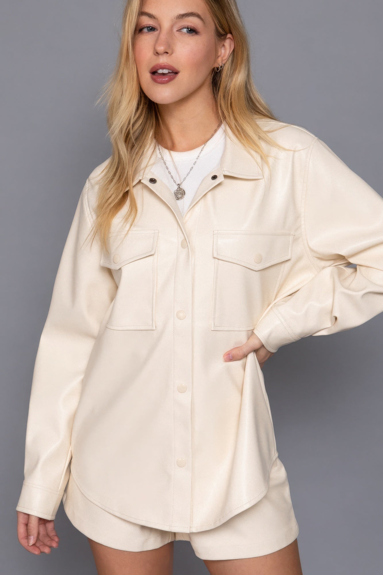 Woman wearing a chic cream faux leather shacket with long sleeves, styled with matching shorts, highlighting a relaxed, versatile look.