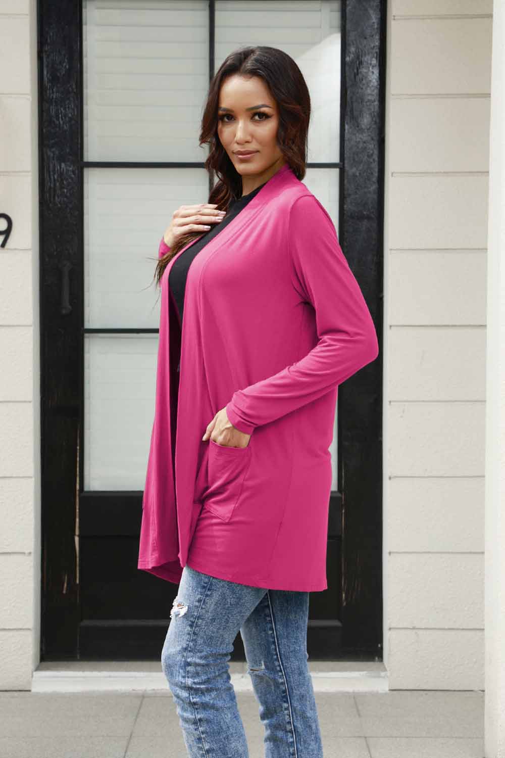 Woman wearing open front long sleeve pink cardigan with pockets over jeans.