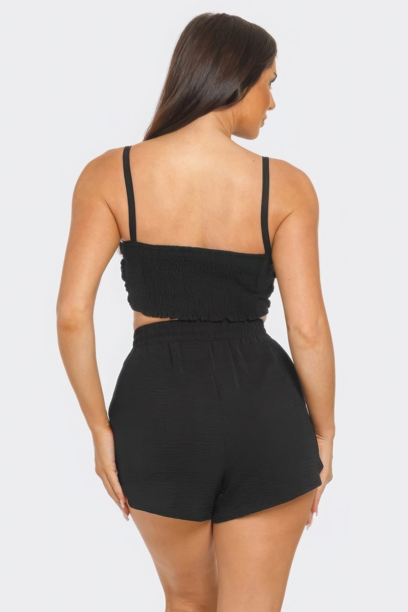 Woman wearing black shorts set with elastic waistband and straps, showcasing back view.