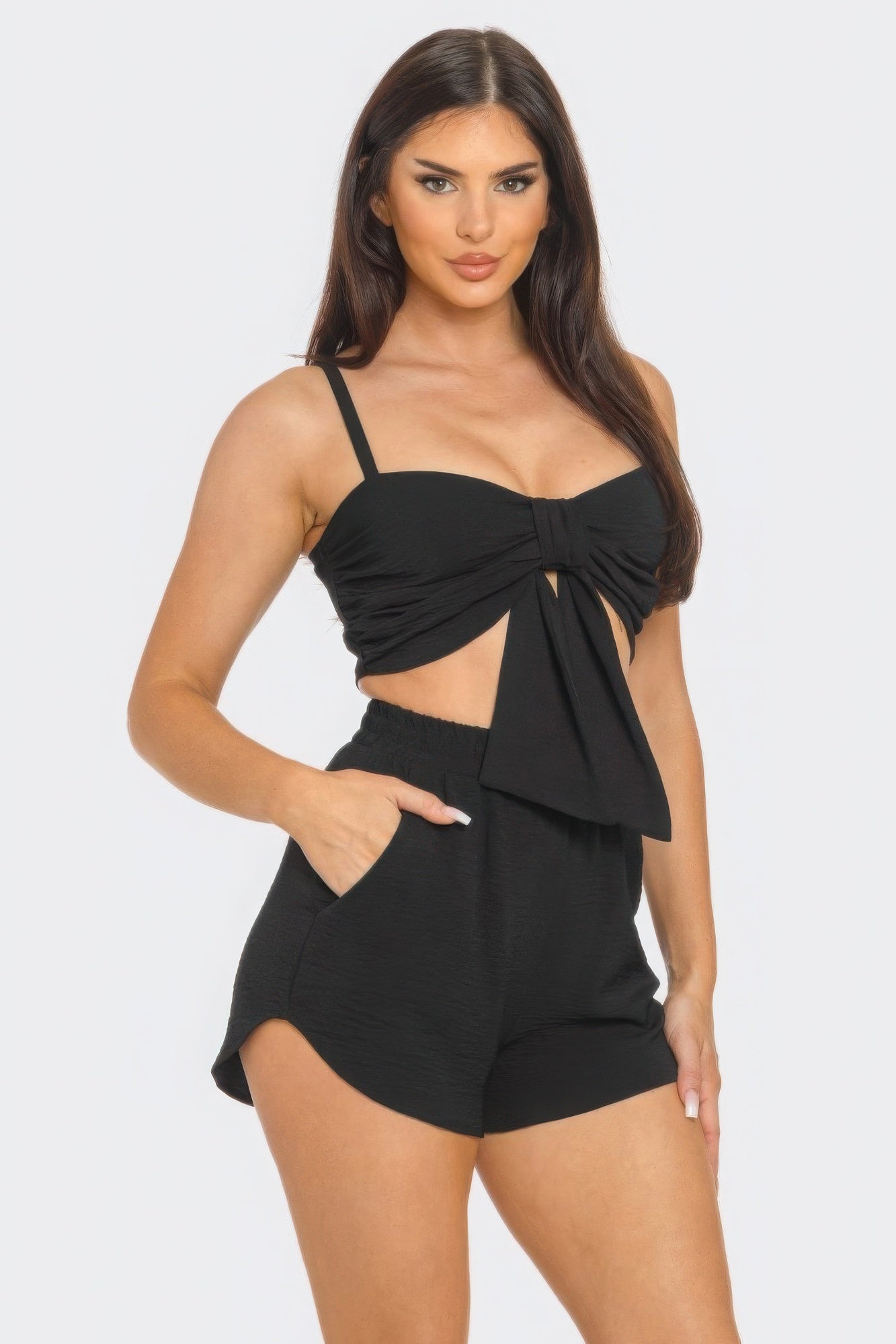 Woman wearing black oversized tie top and shorts set with front bow and twisted tie back, featuring elastic waistband and side pockets.