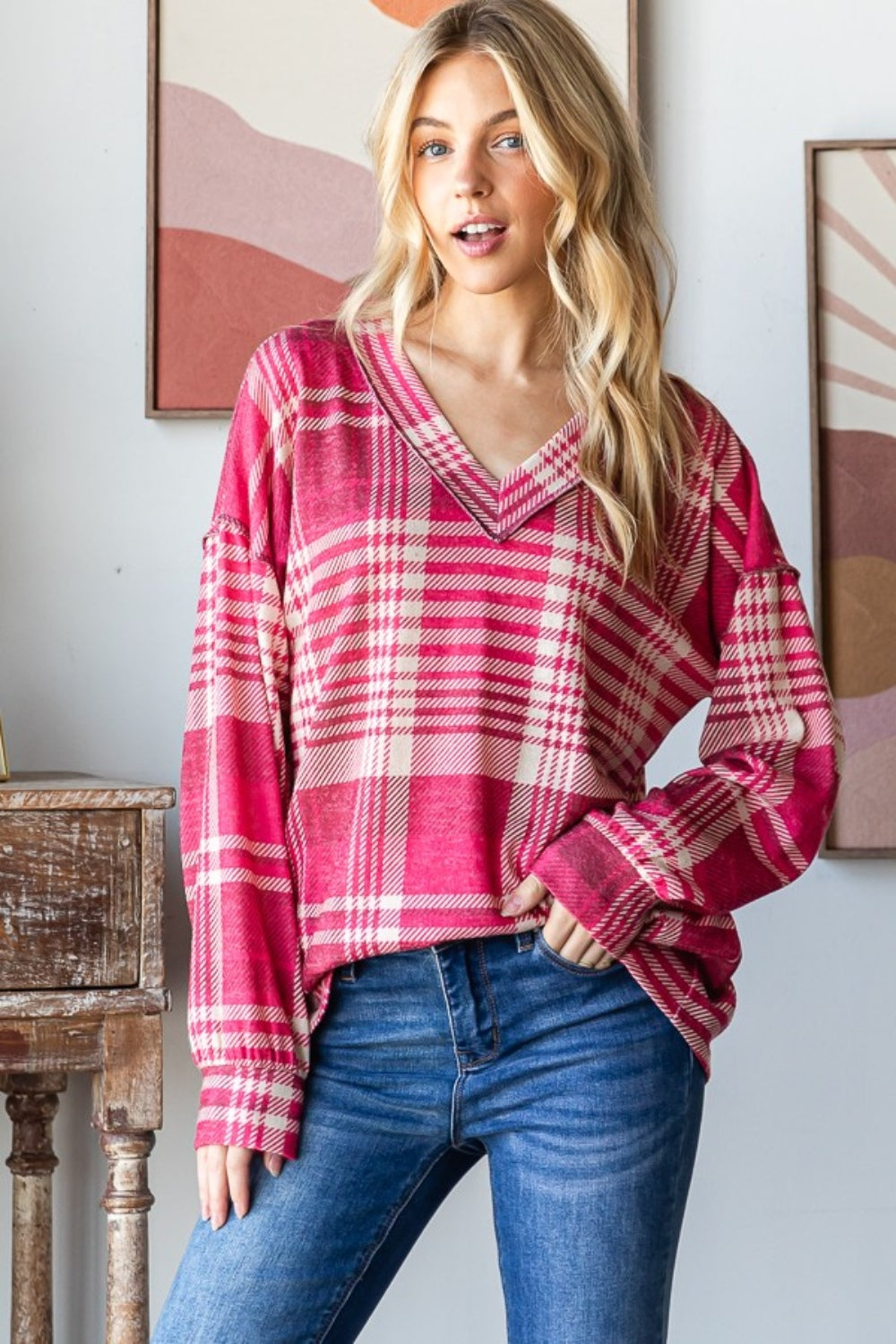 Woman wearing pink plaid drop shoulder V-neck T-shirt with exposed seams and relaxed fit, styled with blue jeans in casual setting.