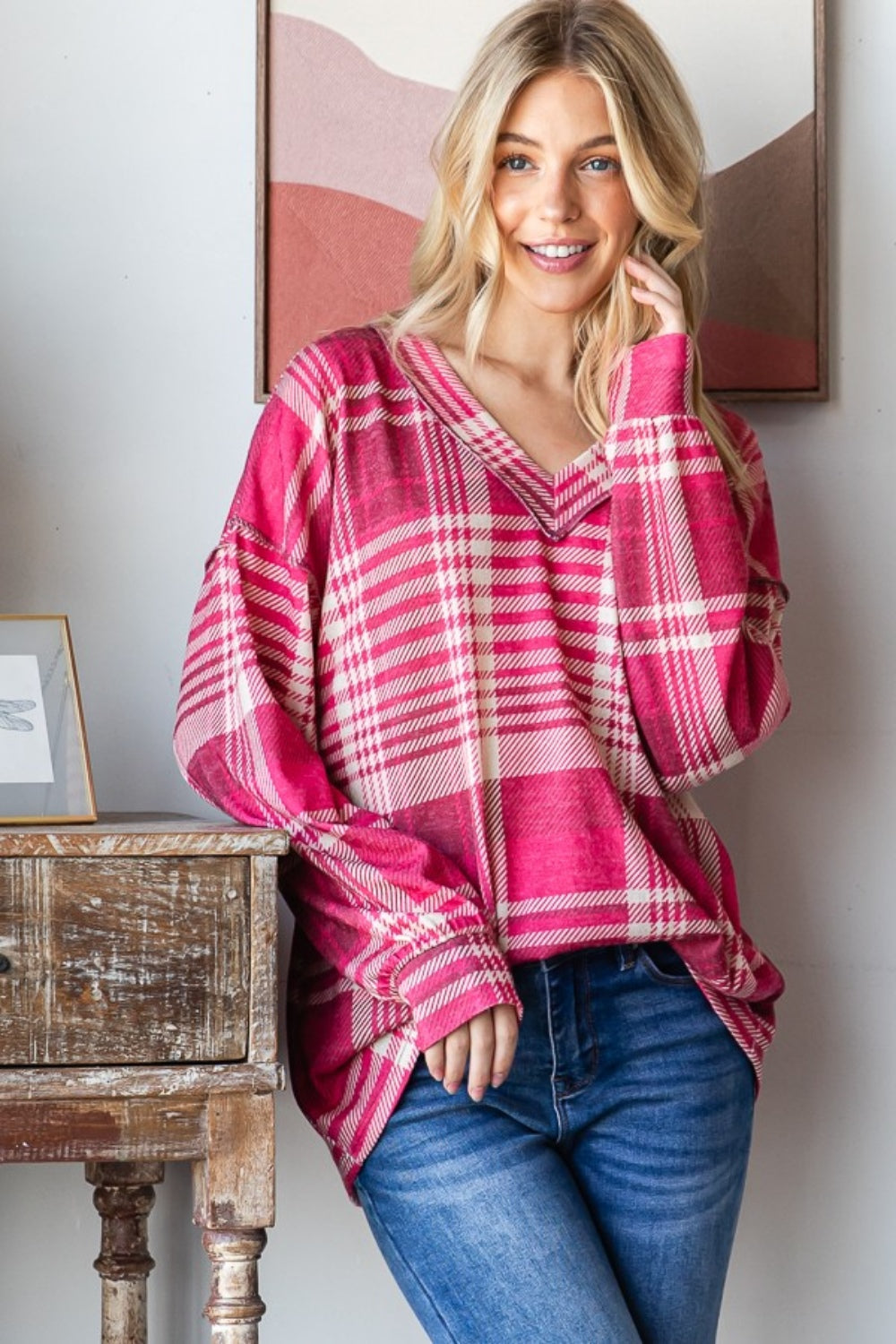 Woman wearing plaid drop shoulder V-neck T-shirt with trendy pattern and relaxed fit, styled with jeans in a cozy indoor setting.