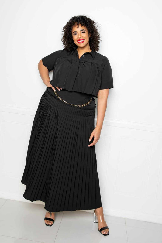 Plus-size model wearing a black pleated cropped shirt and maxi skirt set with a chain belt, showcasing a stylish and elegant look.