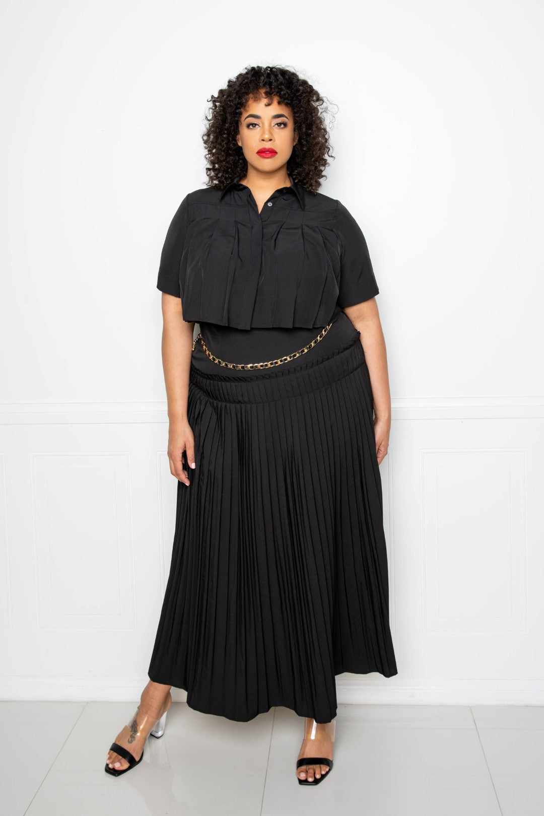 Plus size model wearing black pleated cropped shirt and maxi skirt set, highlighting elegant and stylish fashion choice.