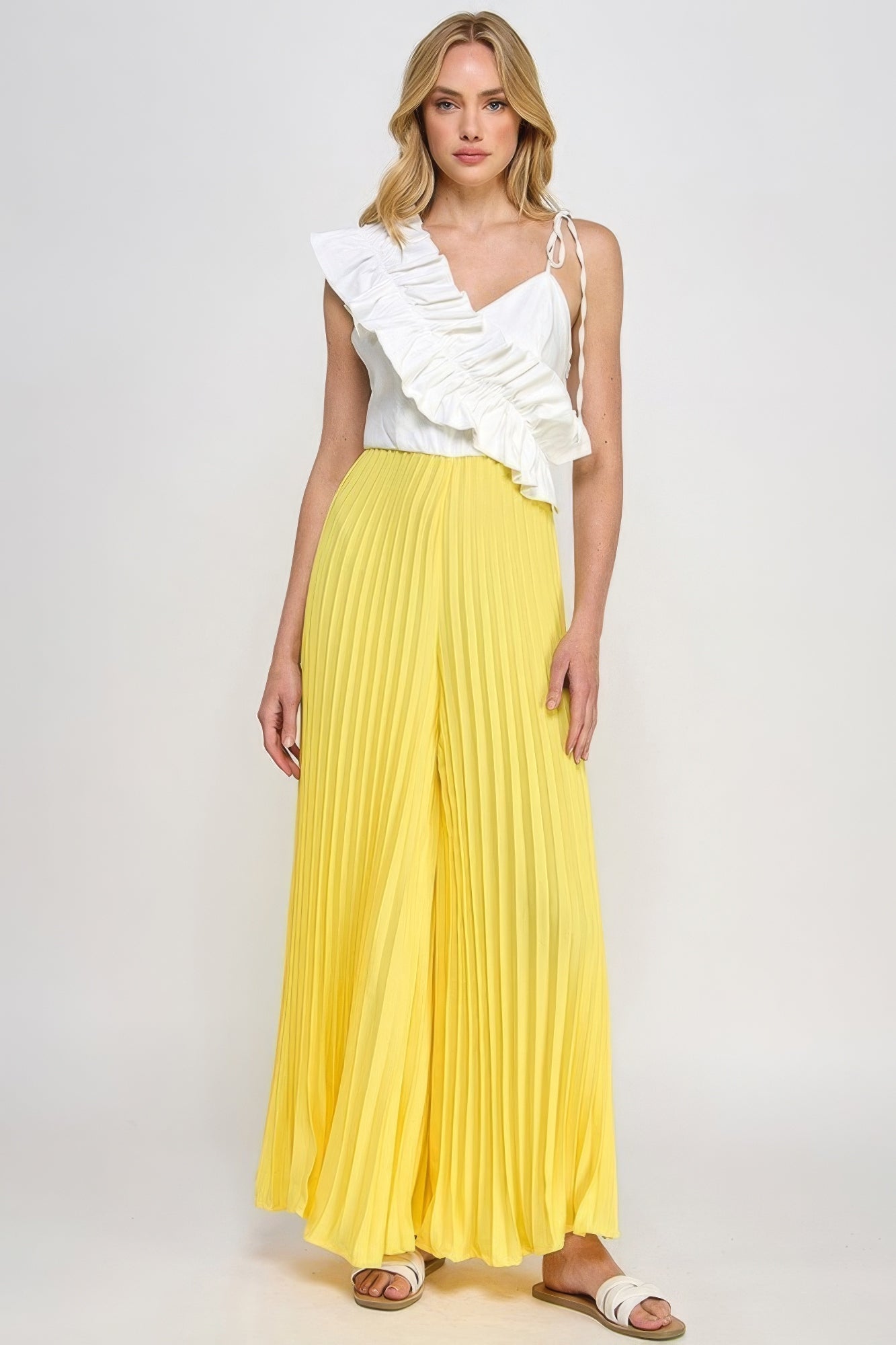 Woman wearing chic pleated cami jumpsuit with asymmetrical ruffle detail in yellow and white, polyester, suitable for casual wear