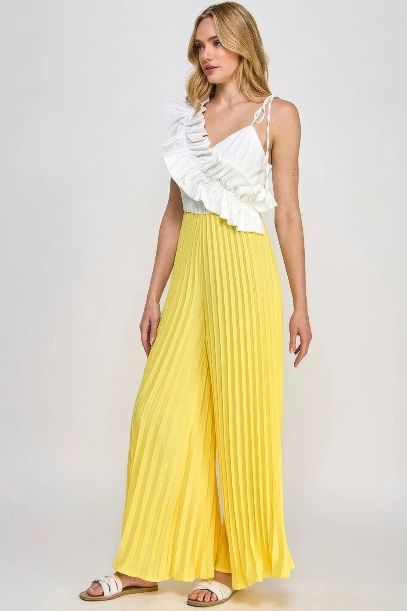 Women's chic pleated cami jumpsuit with white ruffle detailing and yellow pleated bottoms, perfect for contemporary fashion.