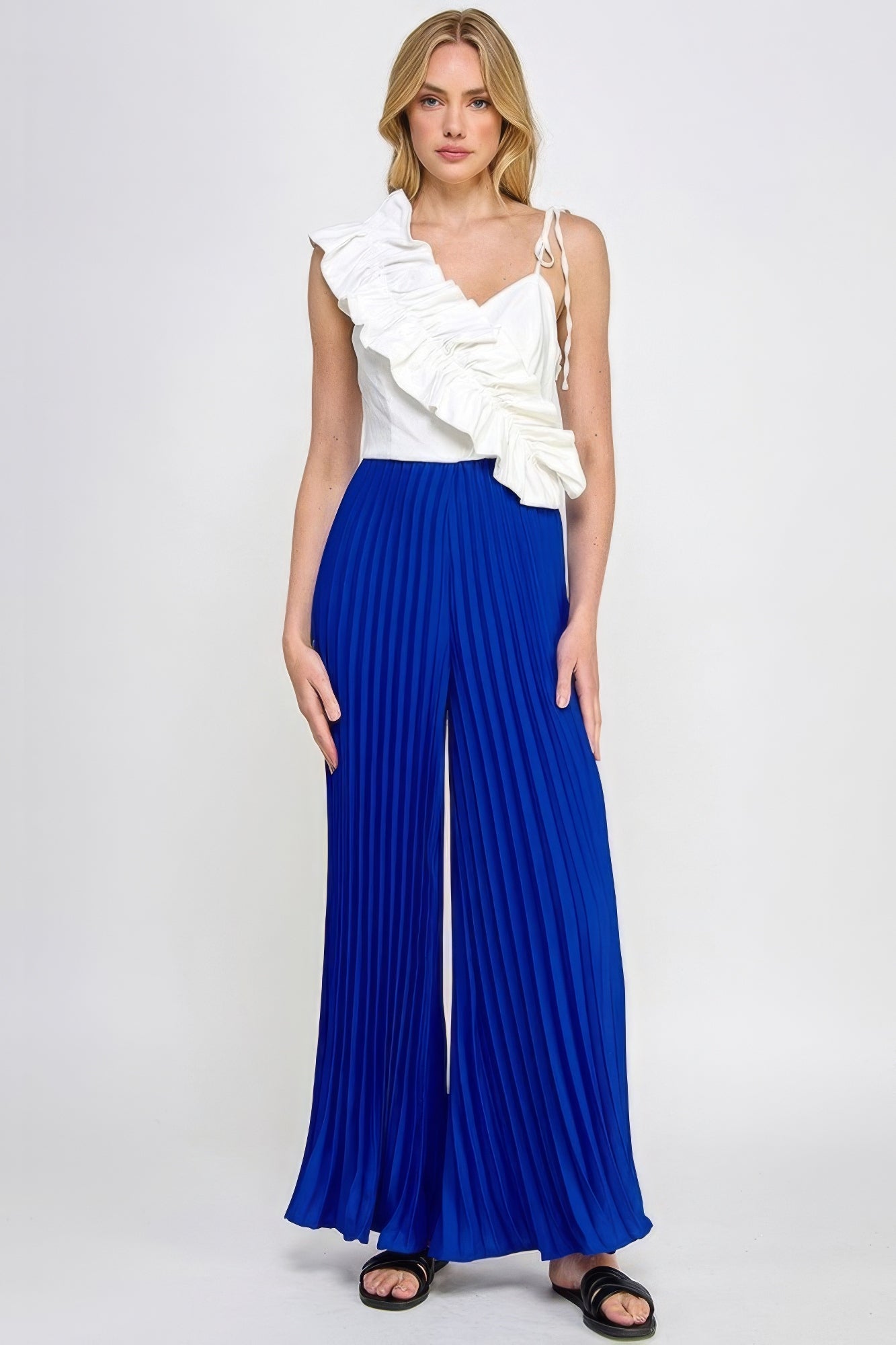 Women's white and blue pleated cami jumpsuit with asymmetrical ruffle detail, showcasing a chic contemporary design.