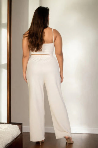 Woman wearing cream bustier cami top and straight pants, stylish plus-size outfit, back view in a softly lit room.