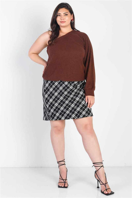 Plus size model wearing brown ribbed one shoulder top with cuffed sleeve, paired with a black plaid skirt and strappy heels.