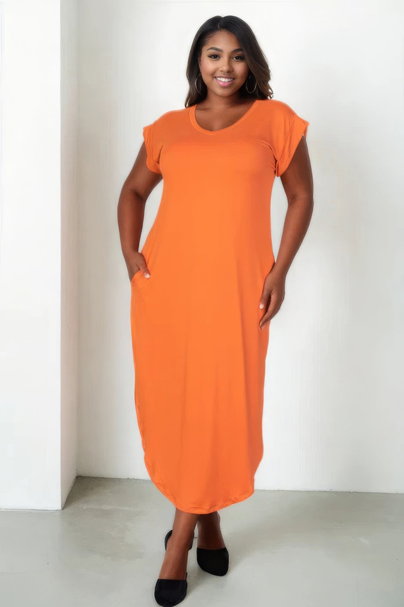 Plus size woman in orange maxi dress with short sleeves and pockets, posing confidently against a white background.