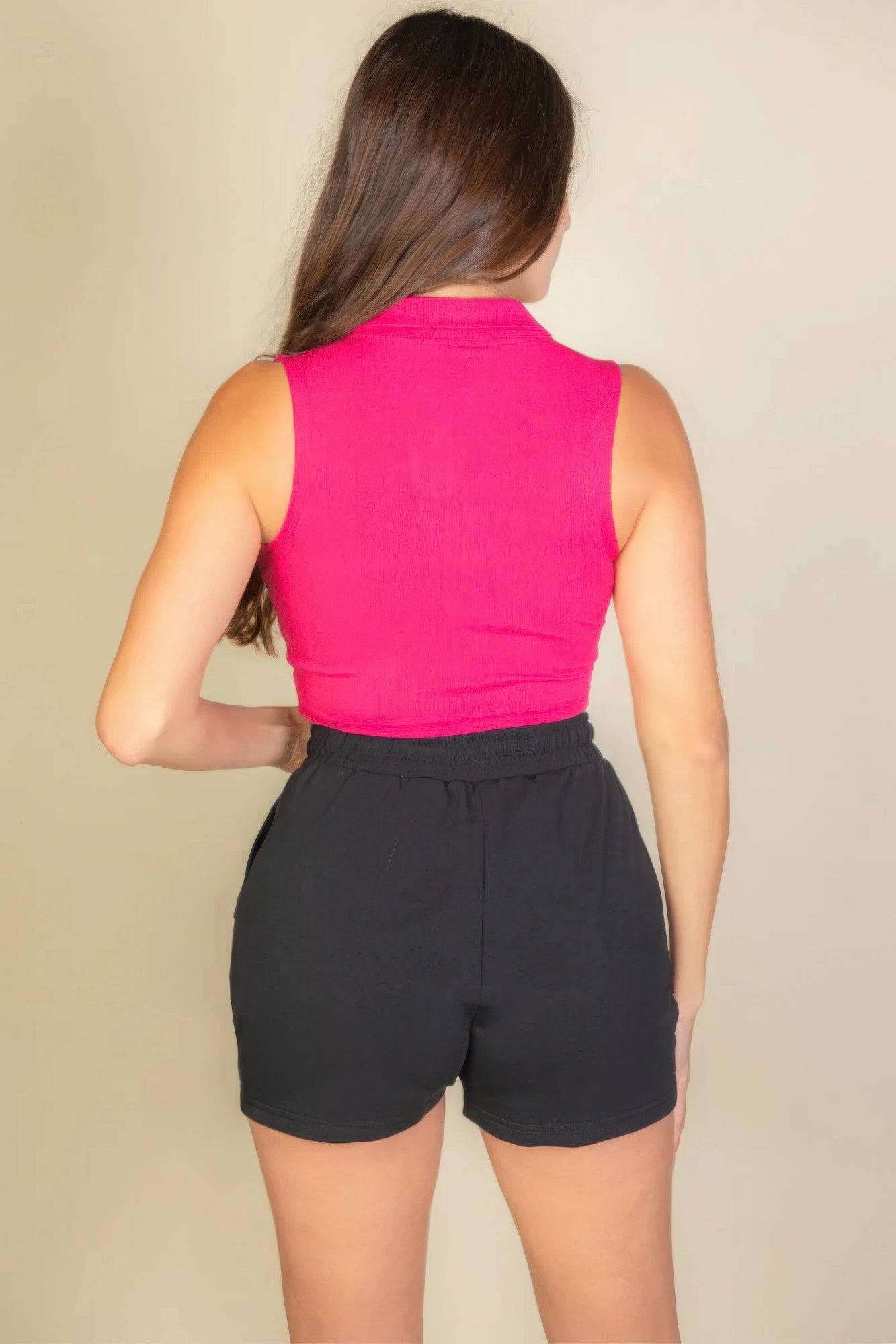 Woman wearing a solid ribbed polo neck tank top in vibrant pink with black shorts, showcasing a sleek and streamlined silhouette.