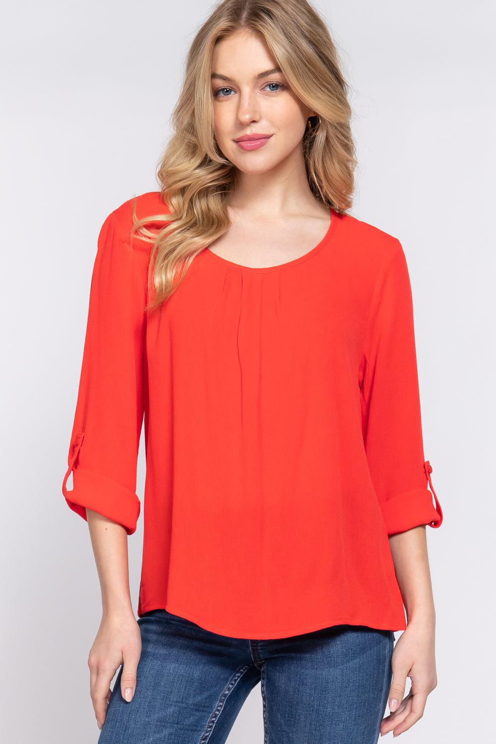 Woman wearing a tomato red roll up sleeve pleated blouse with a round neck, made of 100% rayon.