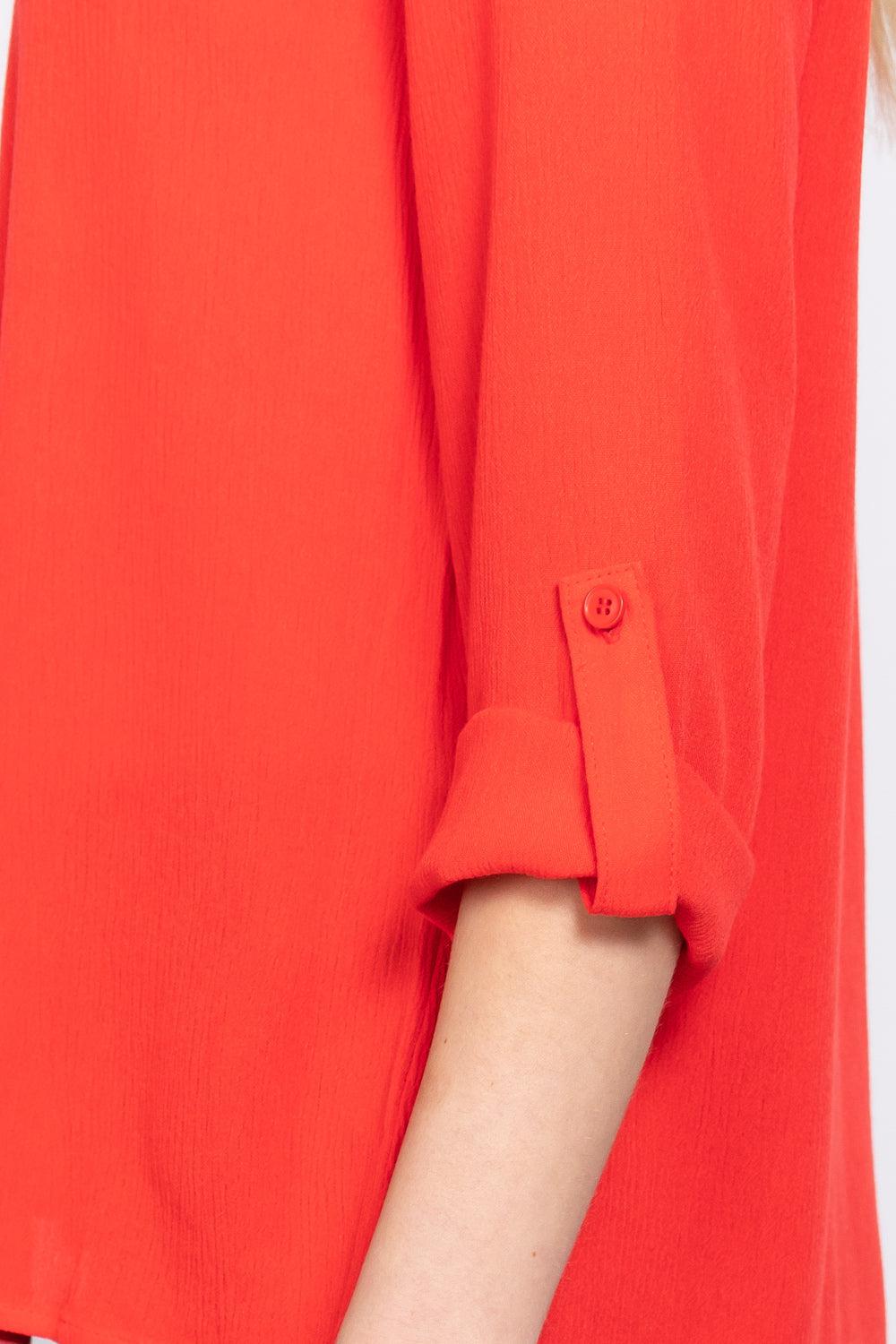 Close-up of a tomato-colored roll-up sleeve blouse with button detail, showcasing pleated fabric and 3/4 sleeve design.