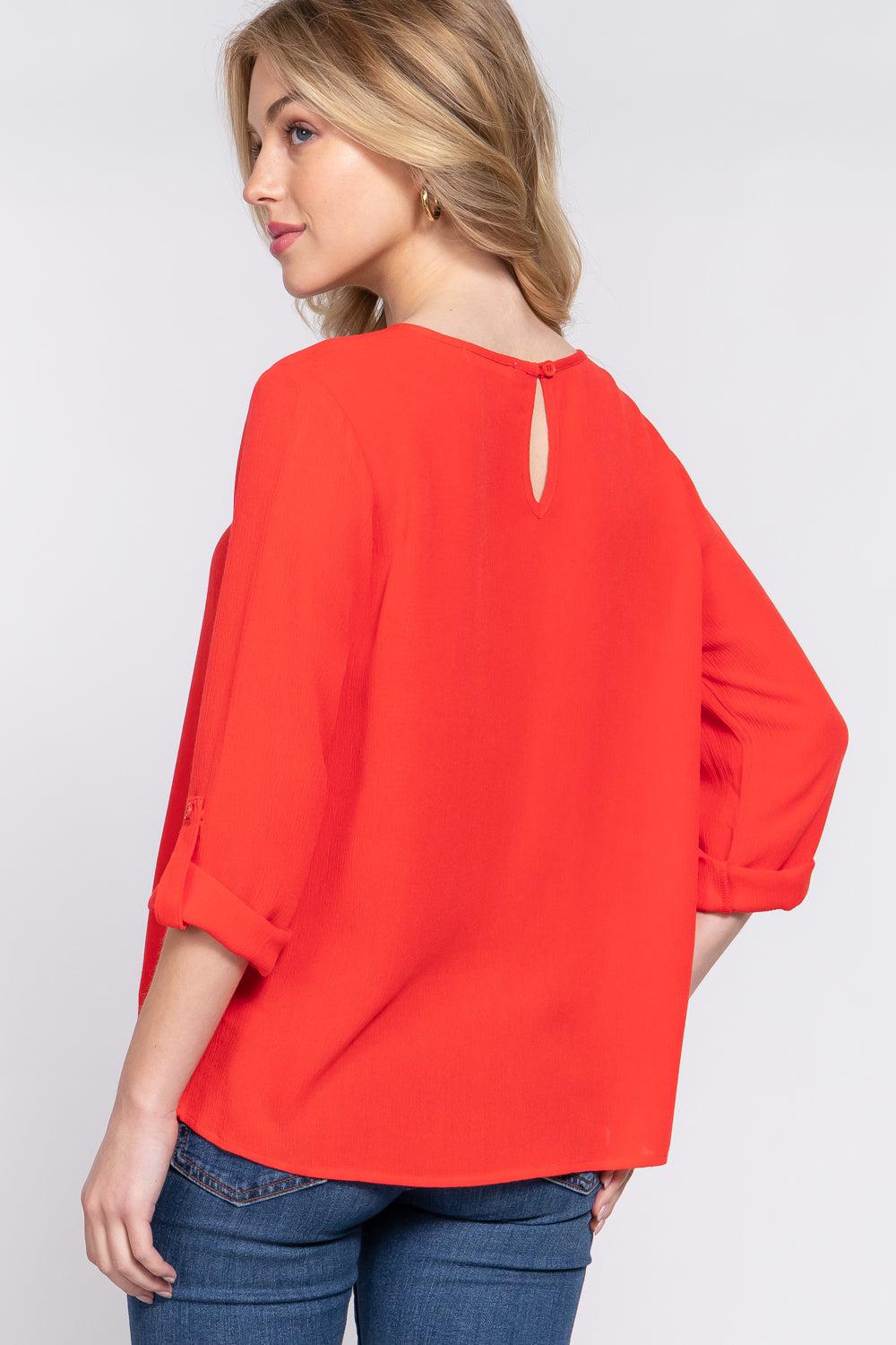 Woman wearing a tomato red roll-up sleeve pleated blouse with a round neck, viewed from the back.