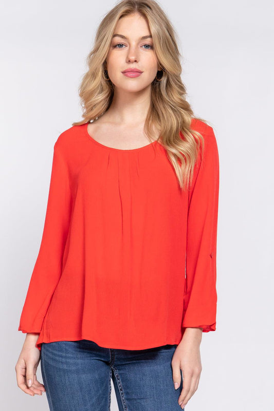 Woman wearing tomato red roll-up sleeve pleated blouse with round neck and 3/4 sleeves, made of 100% rayon.