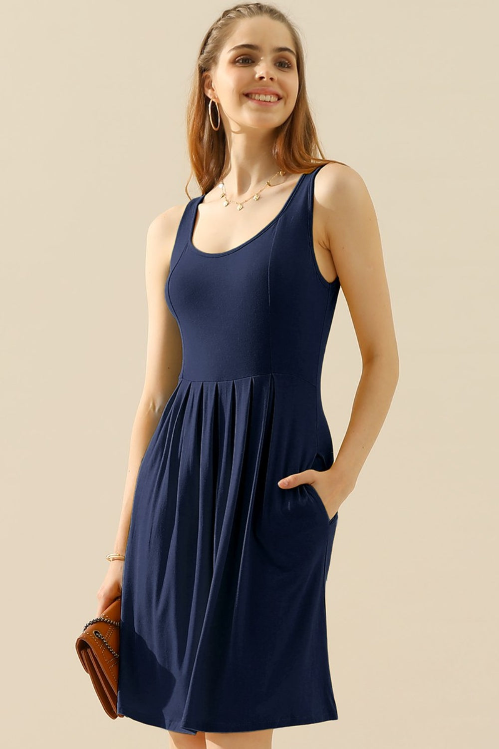 Woman wearing a navy blue round neck ruched sleeveless dress with pockets, showcasing basic style and highly stretchy fabric.