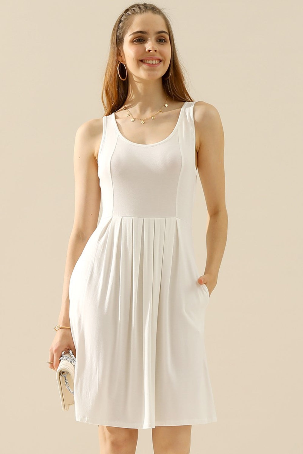 Woman wearing a white round neck ruched sleeveless dress with pockets, made of highly stretchy polyester and spandex material.