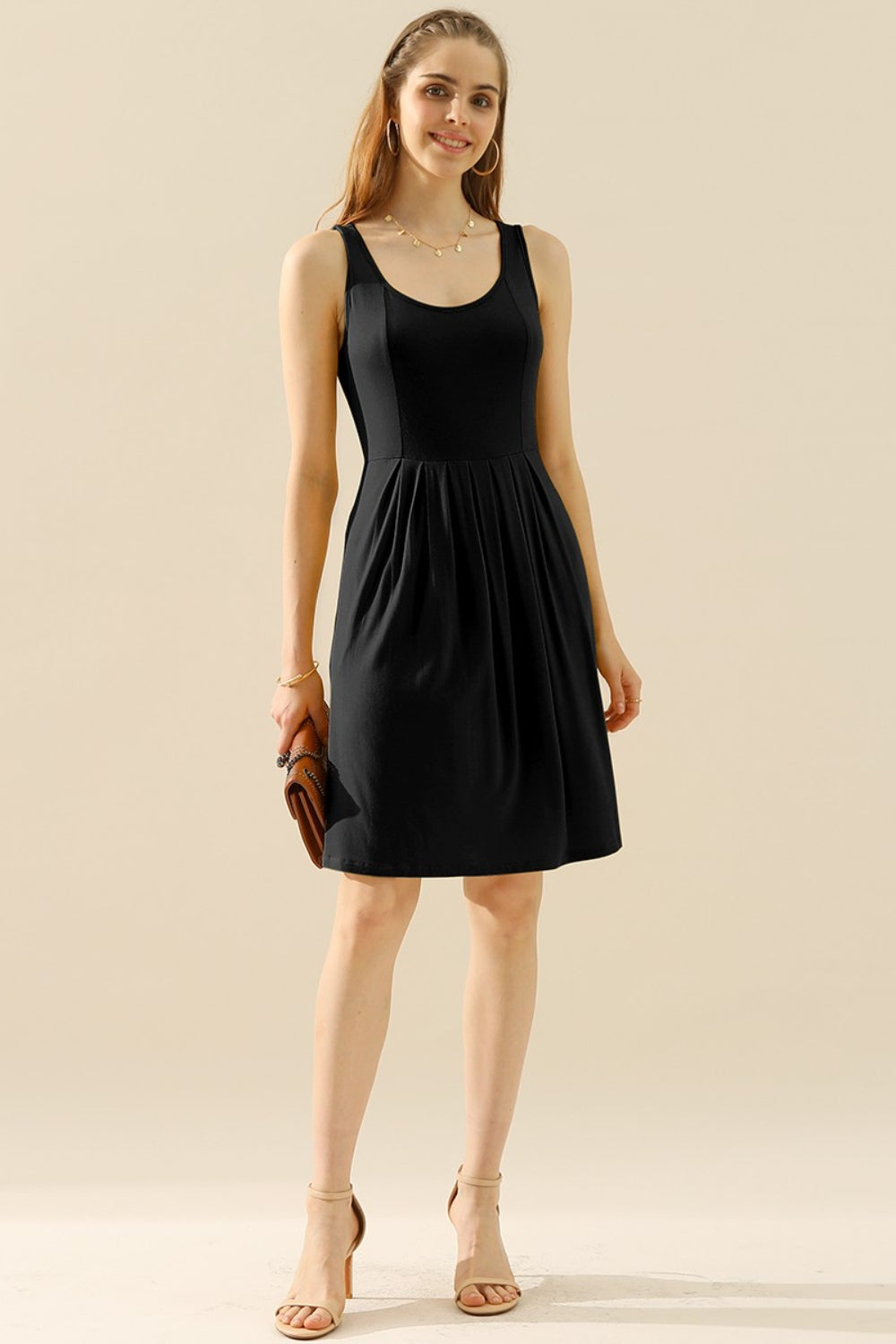 Woman wearing a black round neck ruched sleeveless dress with pockets, featuring a basic style and highly stretchy material.