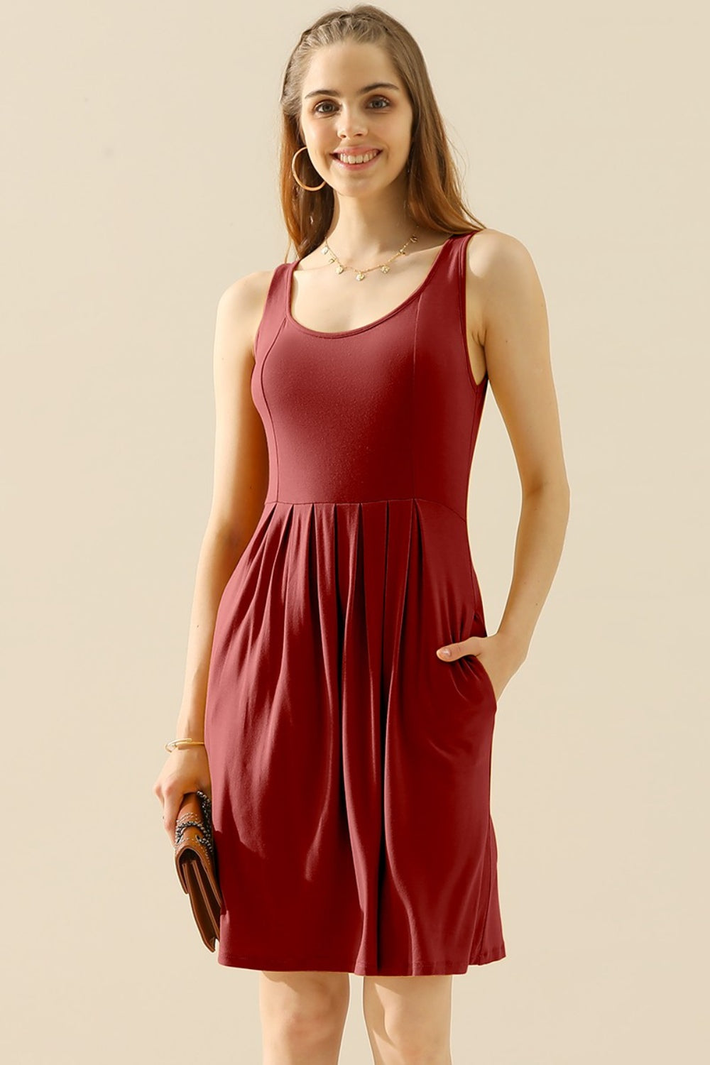 Woman wearing a round neck ruched sleeveless dress with pockets, in a vibrant red color, showcasing a stylish and comfortable fashion look.