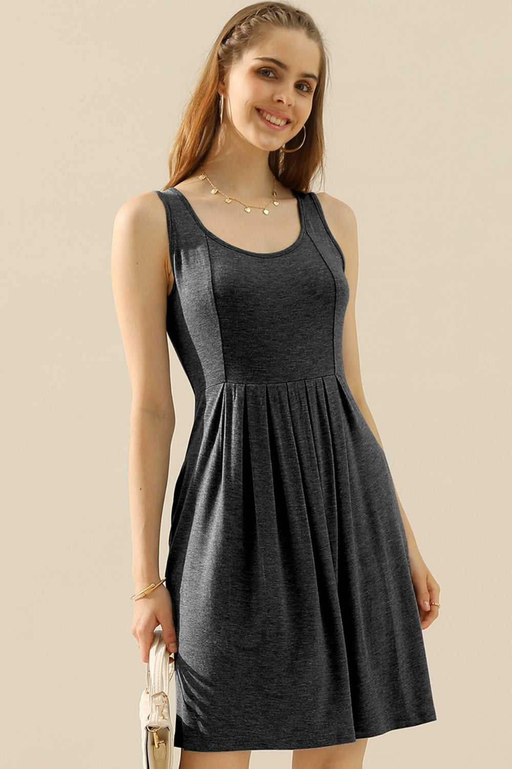 Woman wearing a round neck ruched sleeveless dress with pockets in a dark shade.