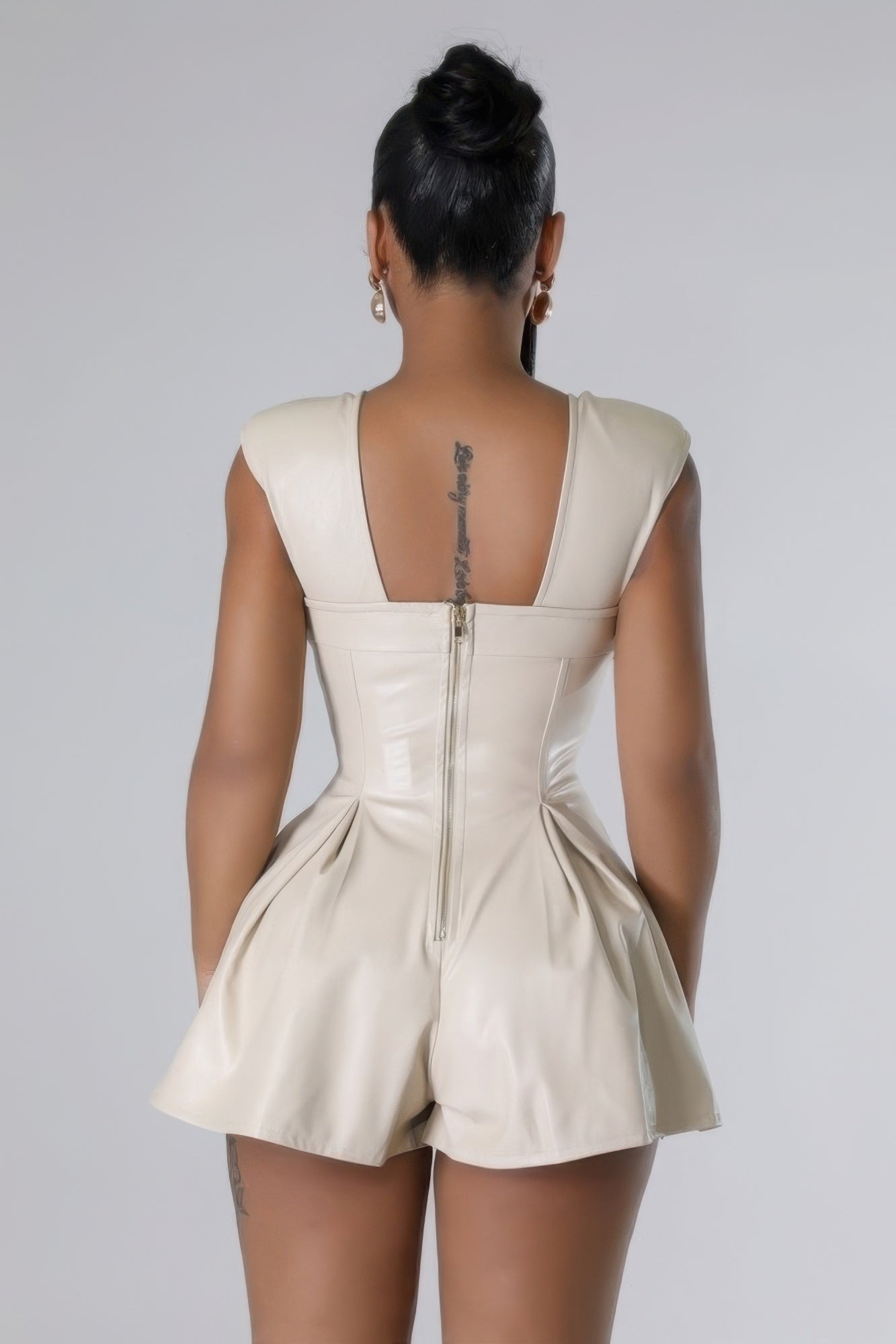 Woman wearing sleeveless faux leather romper with zipper closure in back view, showcasing sleek design and comfort.