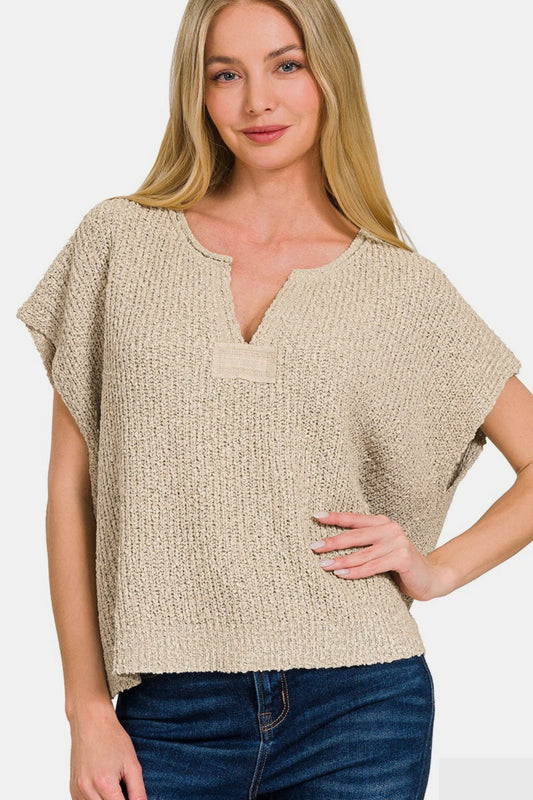 Woman wearing a chic short sleeve side slit sweater in beige, perfect for layering or standalone, paired with jeans for a casual look.