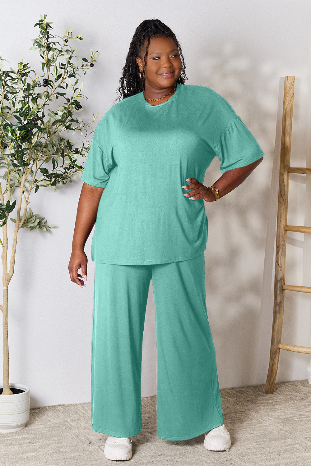 Woman wearing turquoise double take round neck slit top and pants set indoors