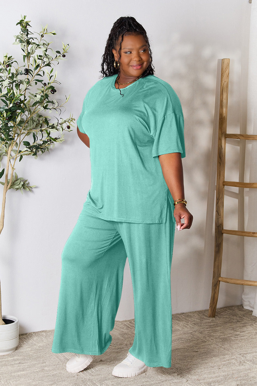 Woman wearing a trendy mint green round neck slit top and pants set in soft rayon blend, standing indoors near a plant.