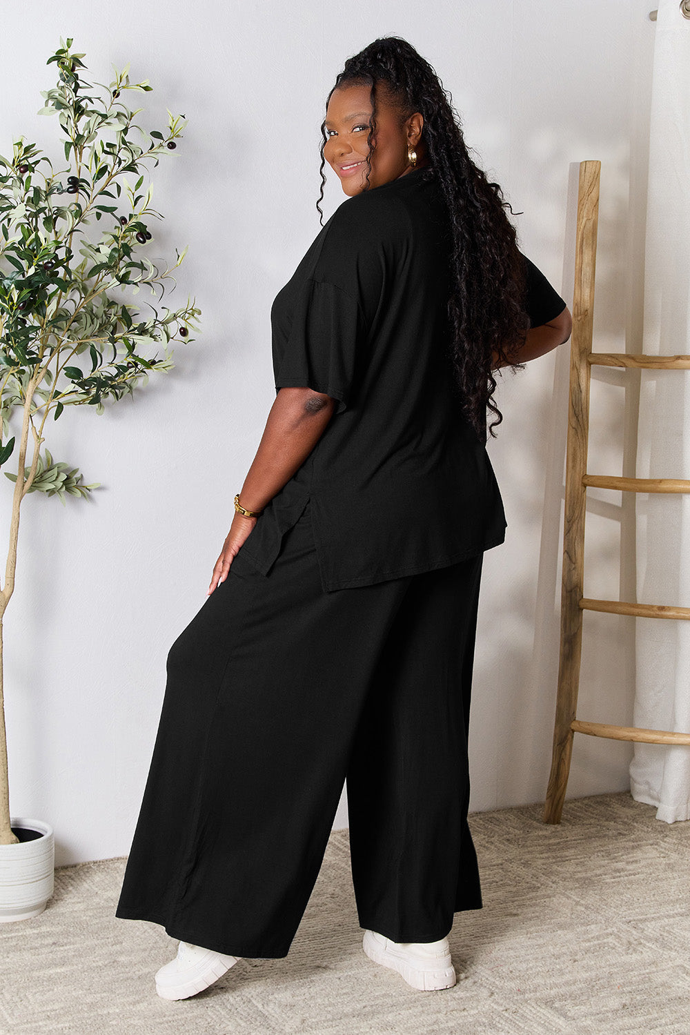 Woman wearing black Double Take round neck slit top and pants set, showcasing trendy two-piece outfit with stylish design.