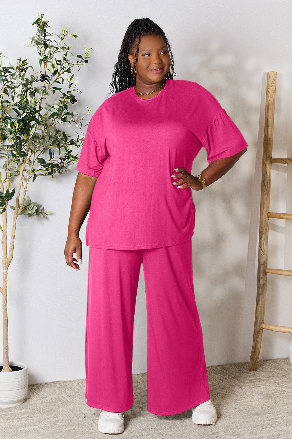 Woman wearing a stylish pink round neck slit top and pants set, made from a soft rayon-spandex blend, standing by a plant.