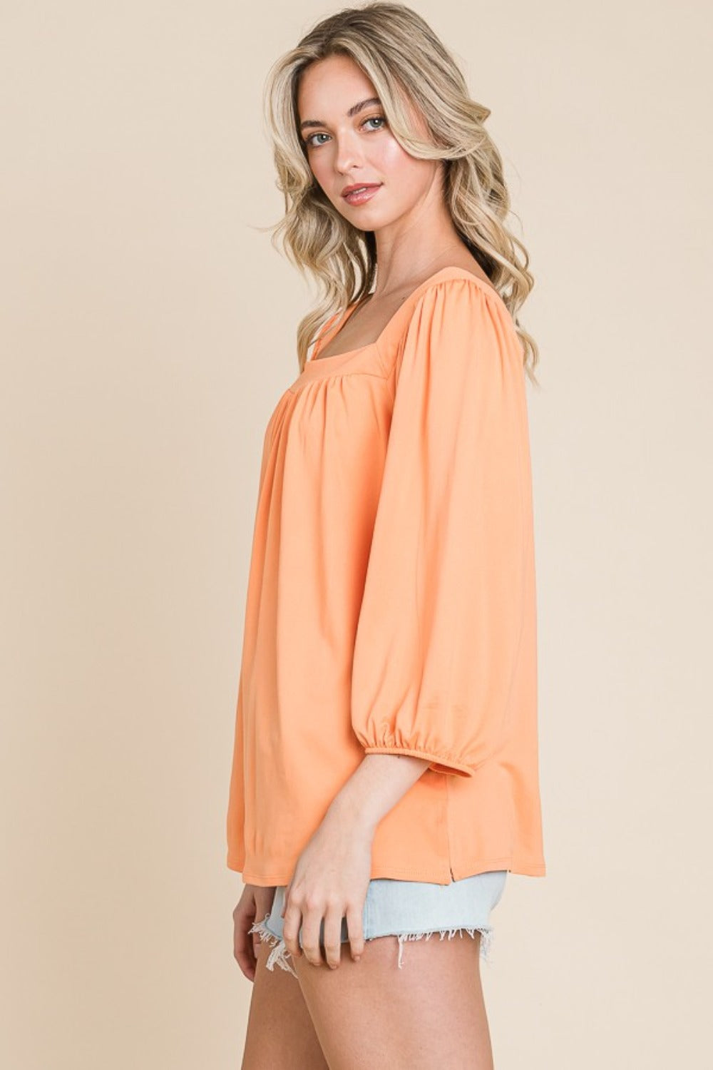 Woman wearing a stylish orange square neck puff sleeve top and denim shorts.