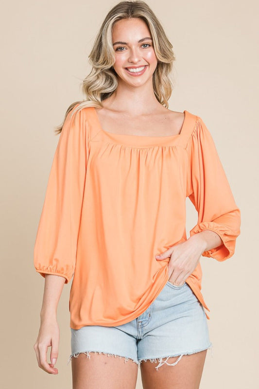 Woman wearing orange square neck puff sleeve top with light denim shorts.