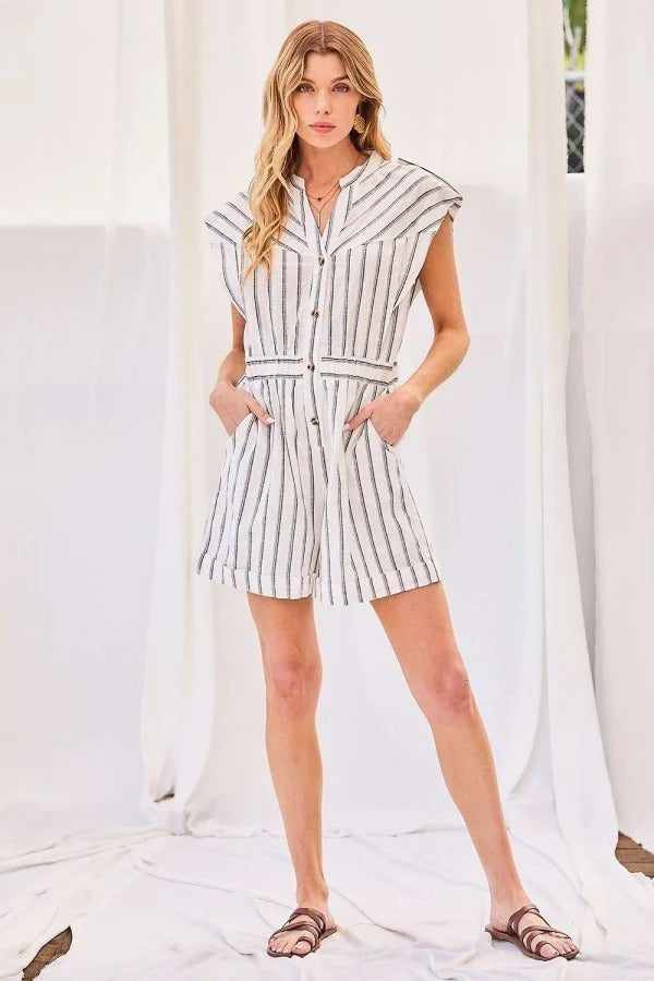 Woman wearing off-white notched neck button elastic waist stripe print romper, 100% rayon, hands in pockets, casual fashion style.