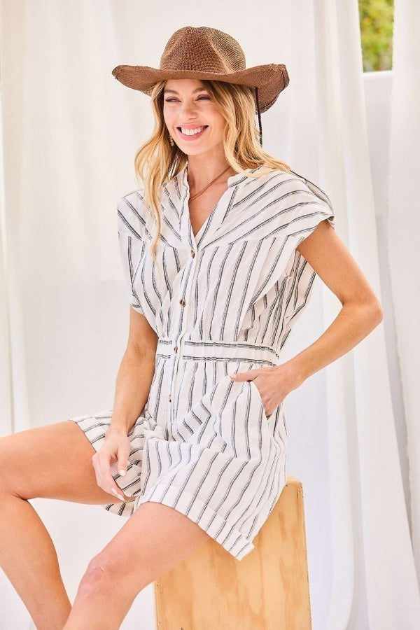 Woman wearing notched neck button romper with elastic waist and stripe print, accessorized with a brown hat, sitting on a stool.