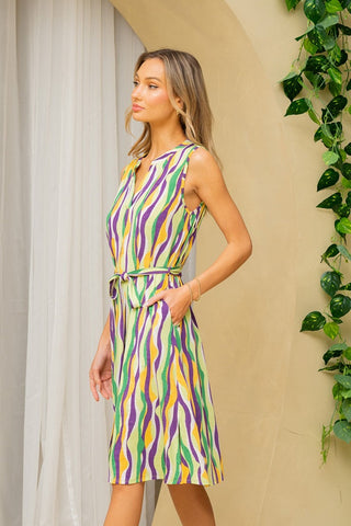 Woman wearing a Sew In Love striped sleeveless dress with tie detail and pockets, surrounded by greenery.