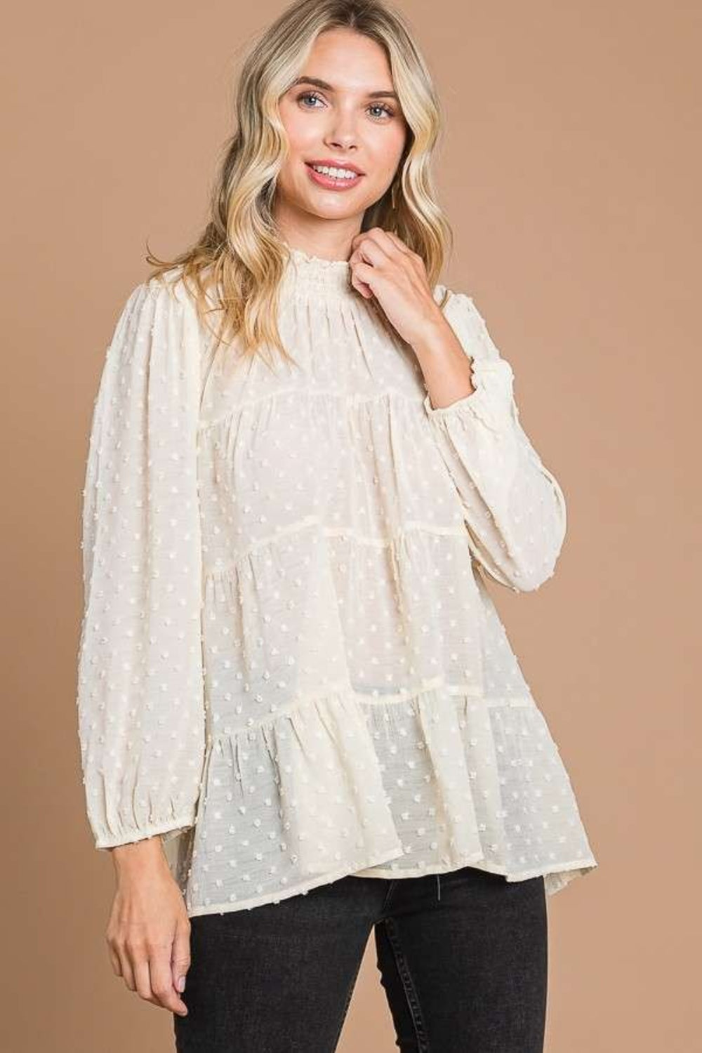 Woman wearing a Swiss Dot Smocked Mock Neck Blouse in ivory with long sleeves, showcasing a chic and feminine style.