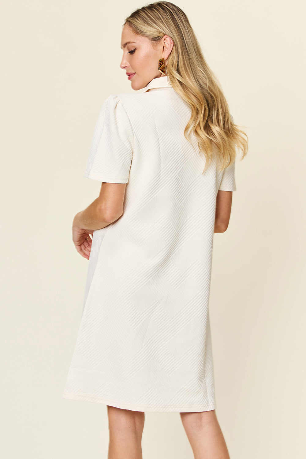 Woman in a texture collared neck short sleeve dress, featuring basic style and slightly stretchy material, facing away.