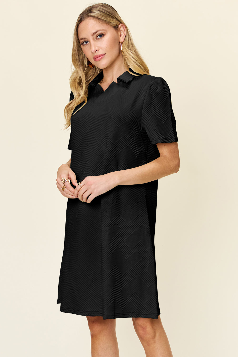 Woman wearing a black texture collared neck short sleeve dress with a slightly stretchy fabric, made from polyester and spandex.