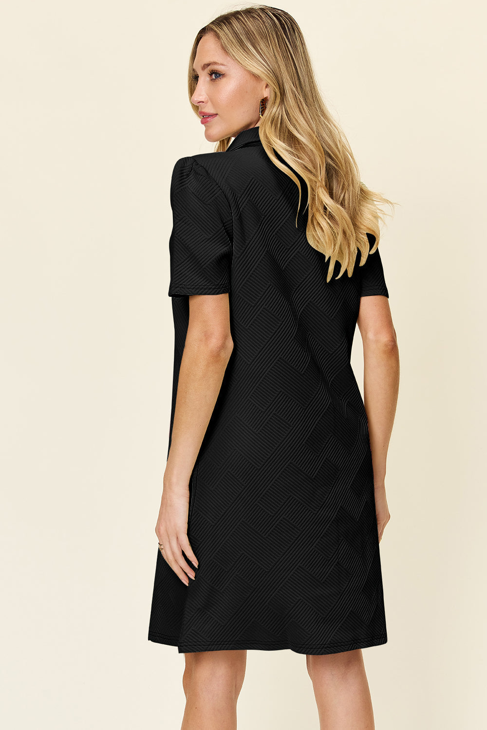 Woman wearing a black texture collared neck short sleeve dress with slight stretch, composed of 98% polyester and 2% spandex.