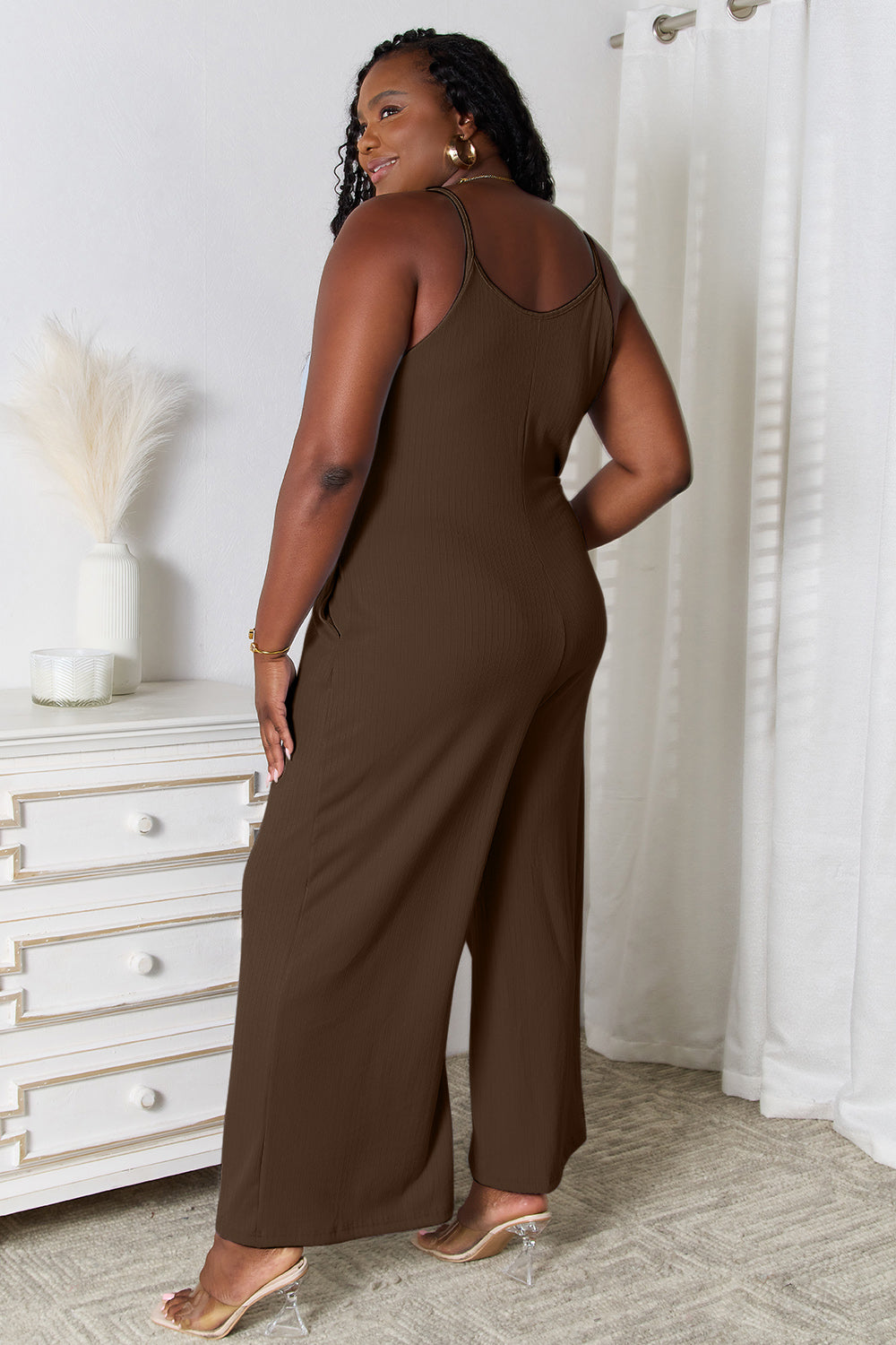 Woman wearing a chic brown V-neck spaghetti strap jumpsuit stands confidently in a stylish room.