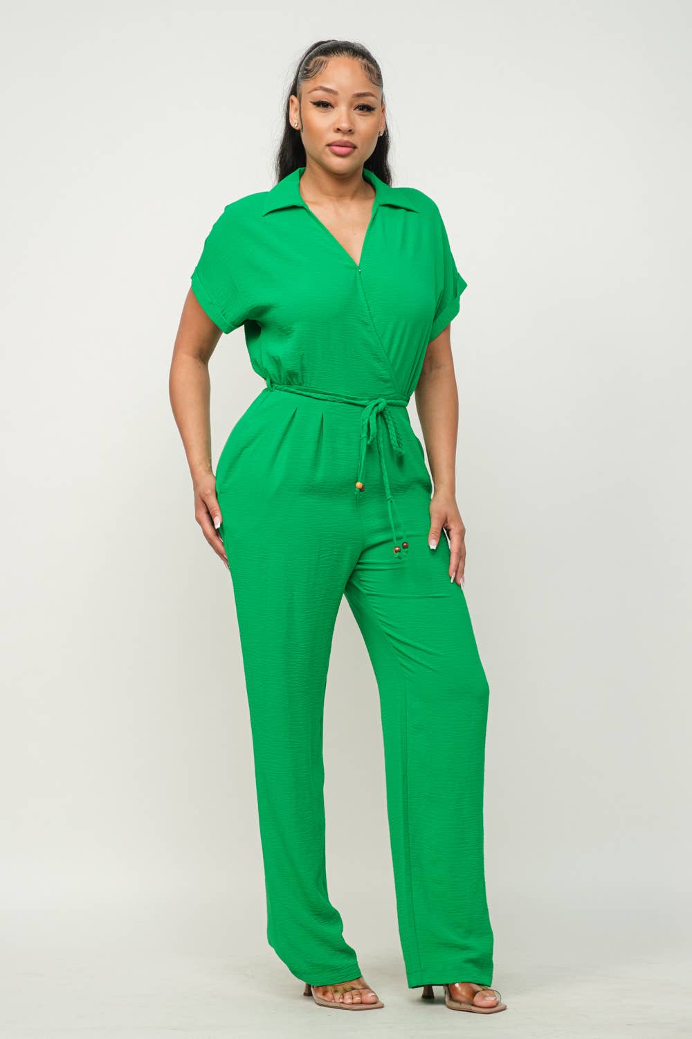 Green open front waist tie jumpsuit with short sleeves, side pockets, and wide leg pants made from Cey Air Flow fabric.