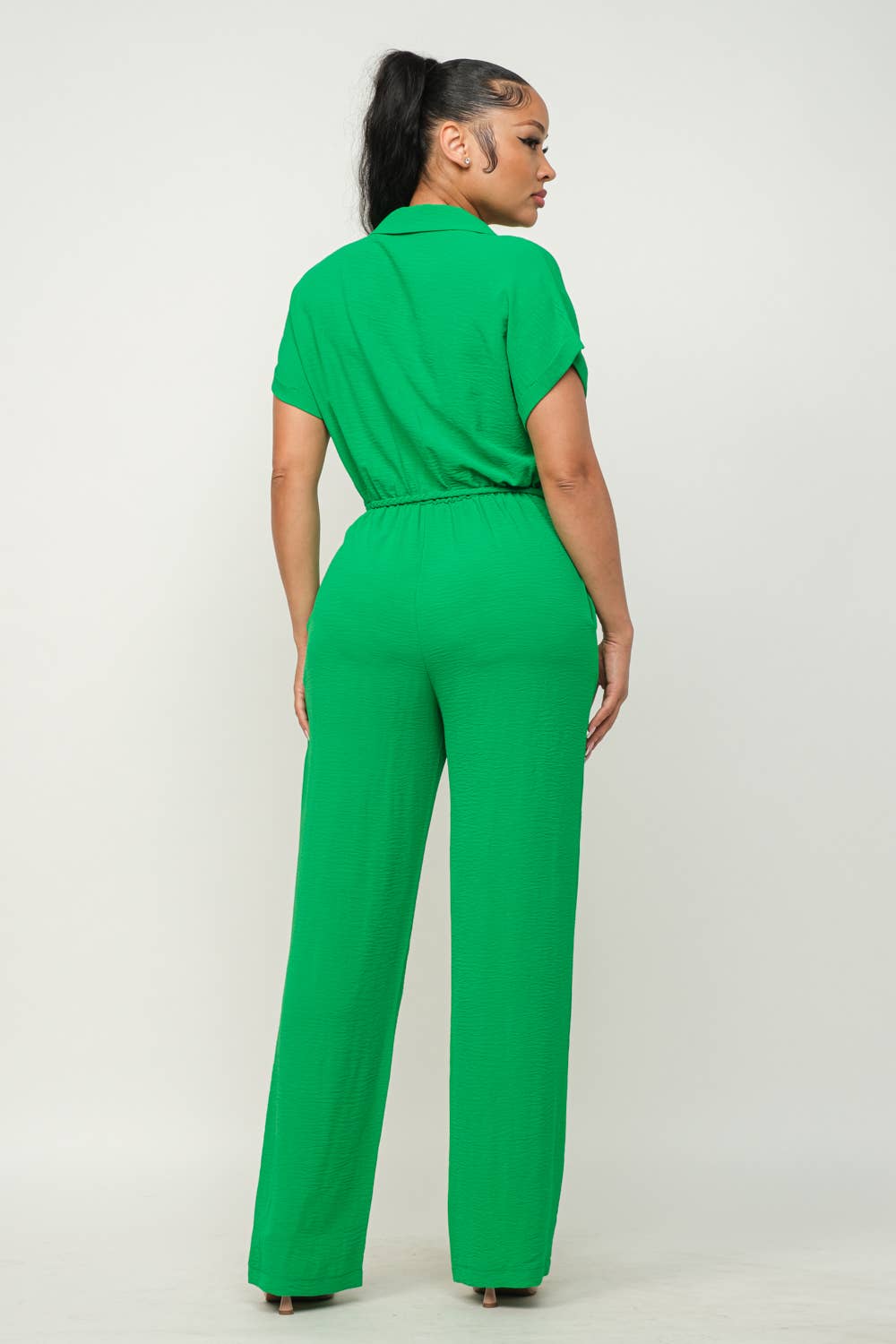 Green jumpsuit with collar, short sleeves, waist tie, elastic shirring, and wide-leg pants viewed from the back.