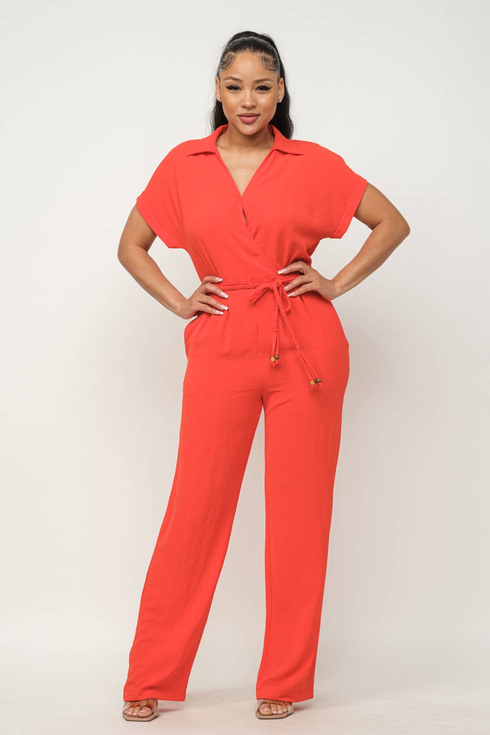 Woman wearing a red open front jumpsuit with waist tie, collared short sleeves, and wide leg pants.