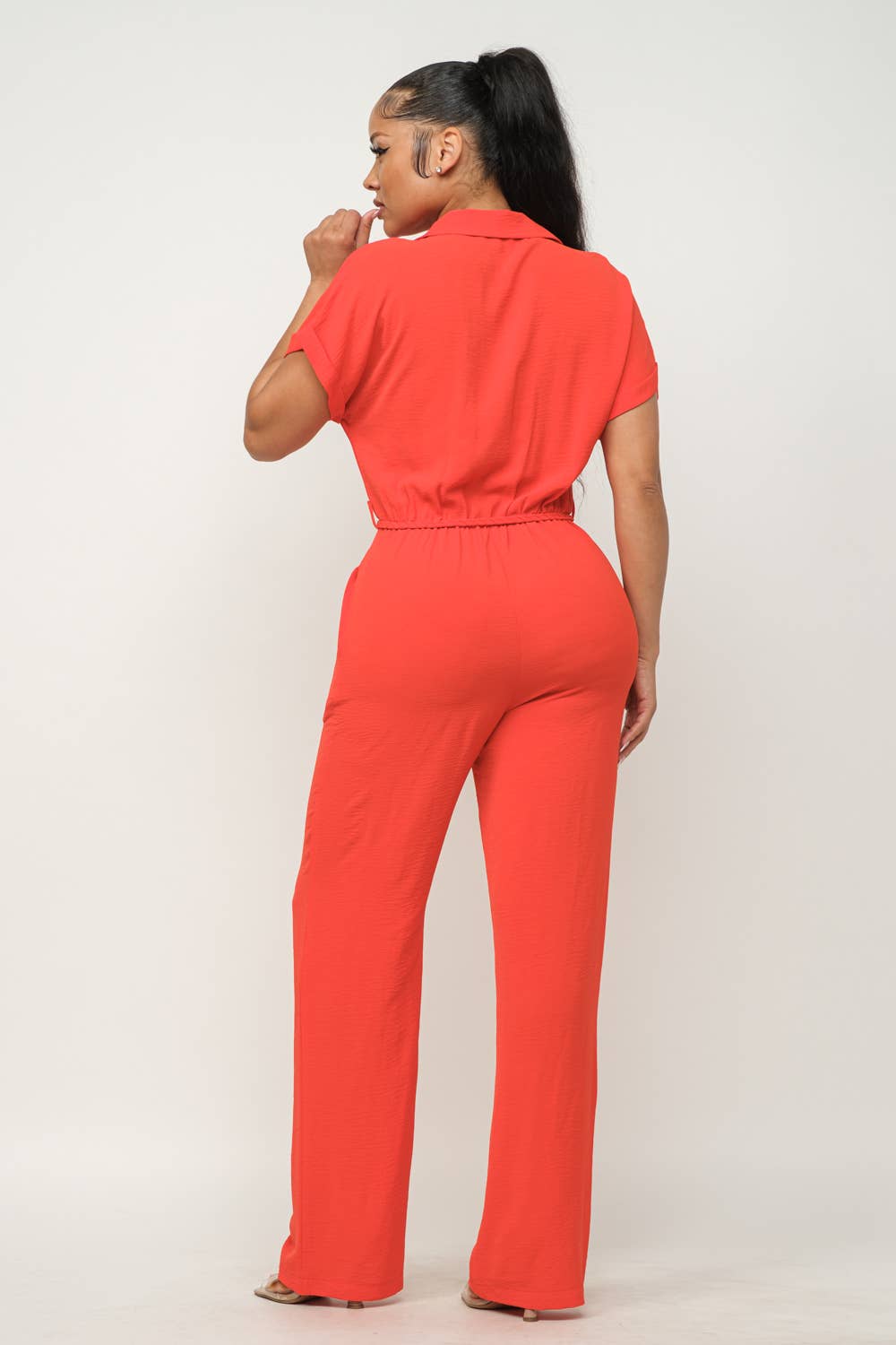 Red open-front jumpsuit with waist tie, collared short sleeves, wide-leg pants, and elastic shirring.