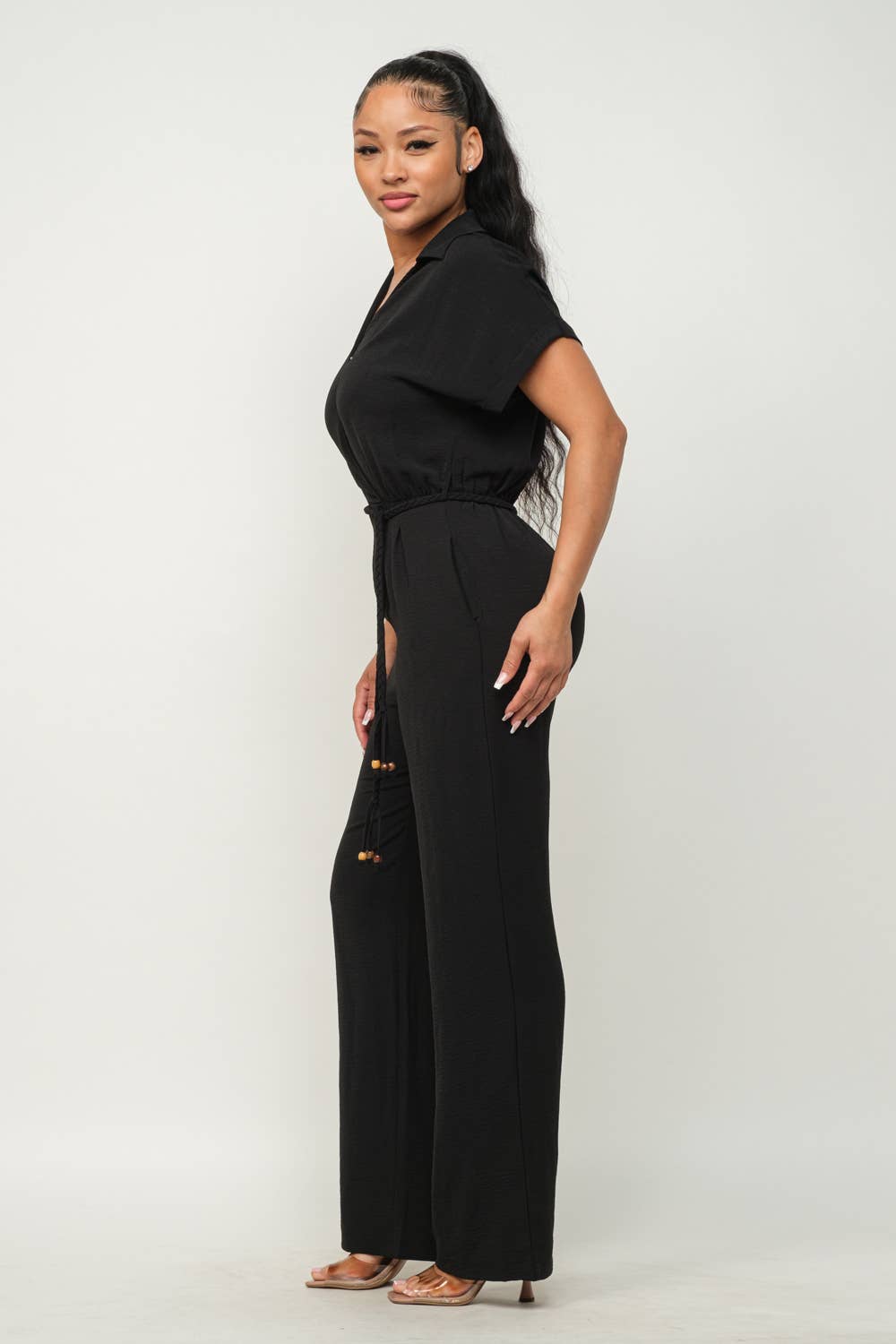 Woman wearing a black open front jumpsuit with waist tie, collared wrap top, and wide-leg pants, showcasing a stylish and elegant look.