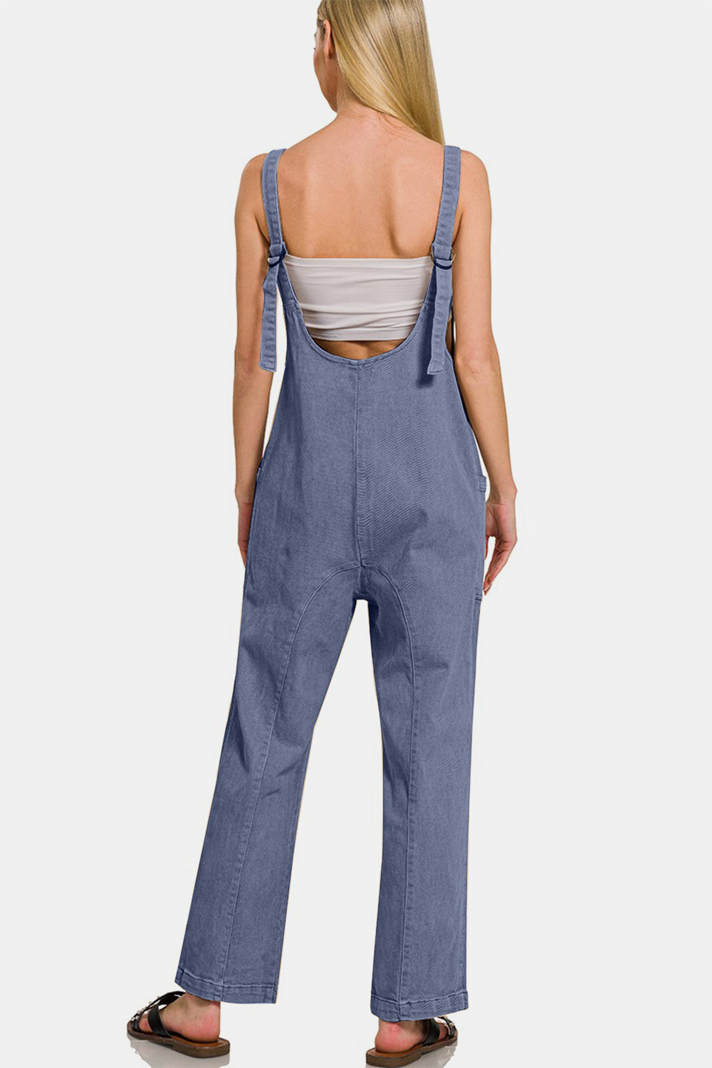 Woman wearing a blue pocketed wide strap jumpsuit with a flowy fit and adjustable straps, back view.