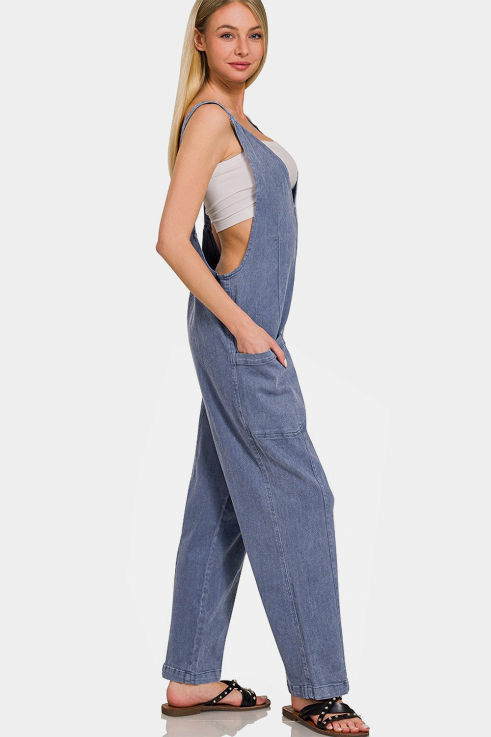 Woman wearing a chic pocketed wide strap jumpsuit in blue denim with a comfy, flowy fit, perfect for versatile styling.