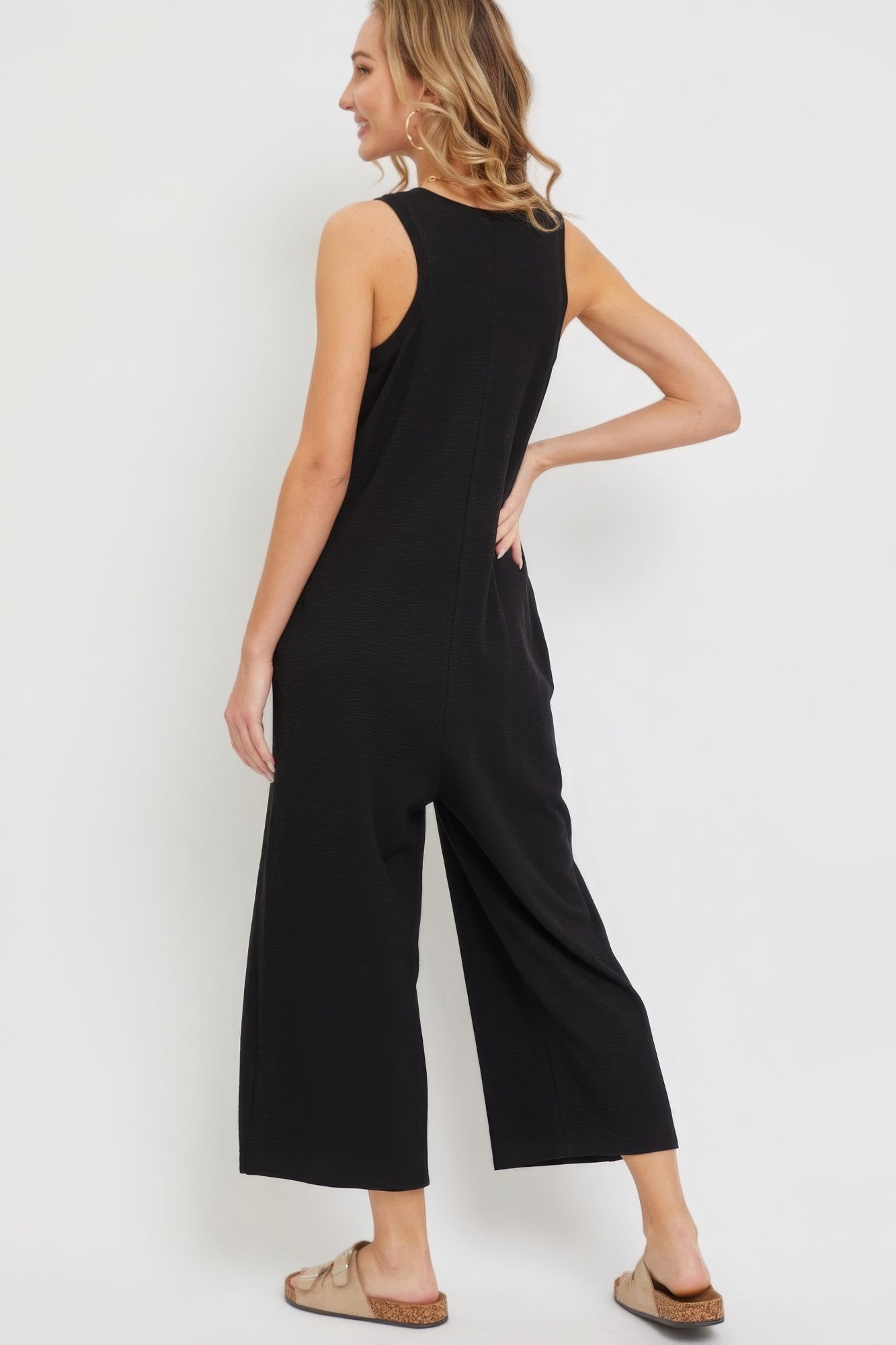 Woman wearing a black sleeveless buttondown jumpsuit with relaxed fit and side pockets, showcasing a chic and comfy style.