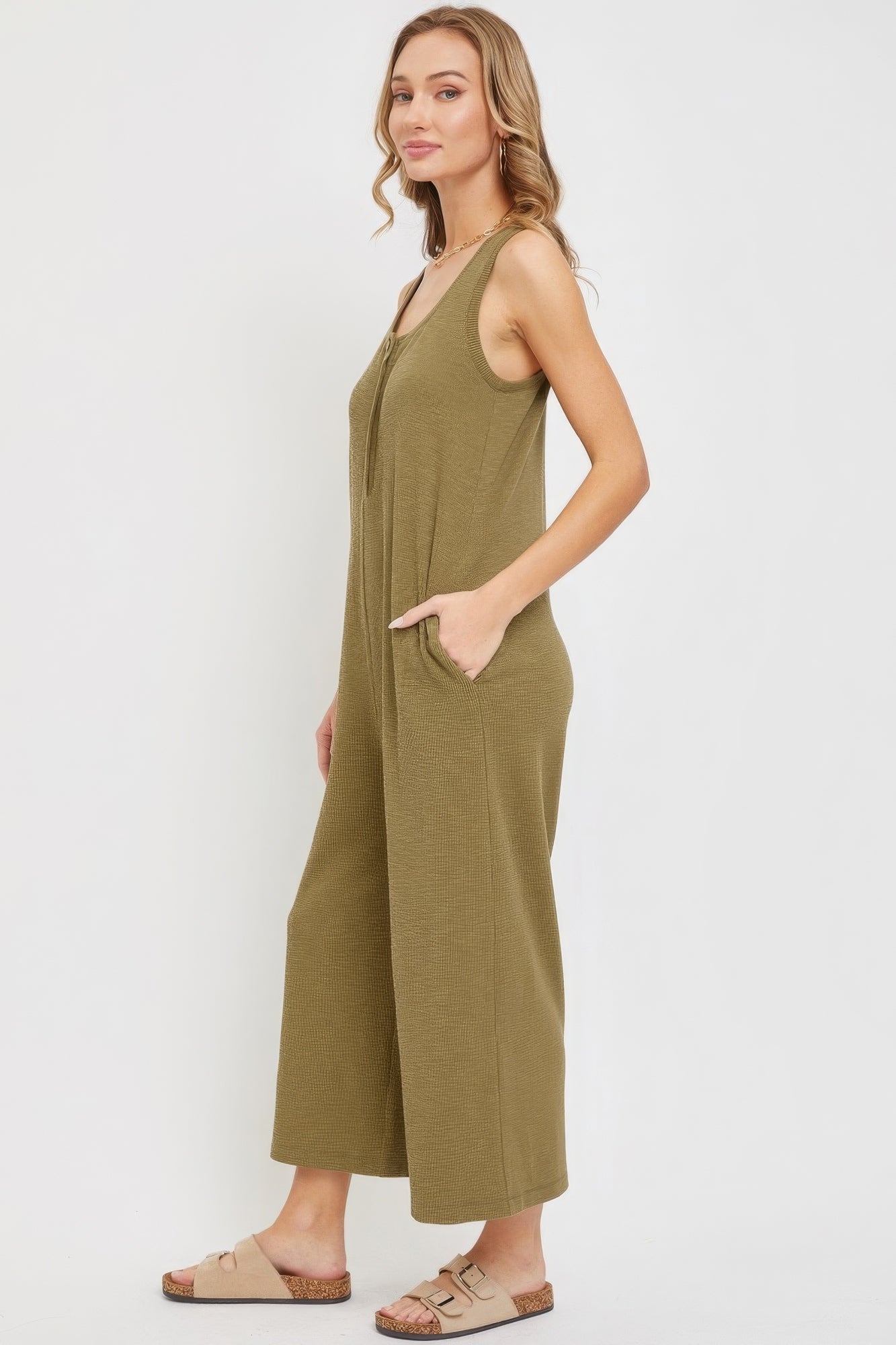 Woman in green sleeveless buttondown jumpsuit with side pockets, demonstrating relaxed fit and slouchy silhouette.