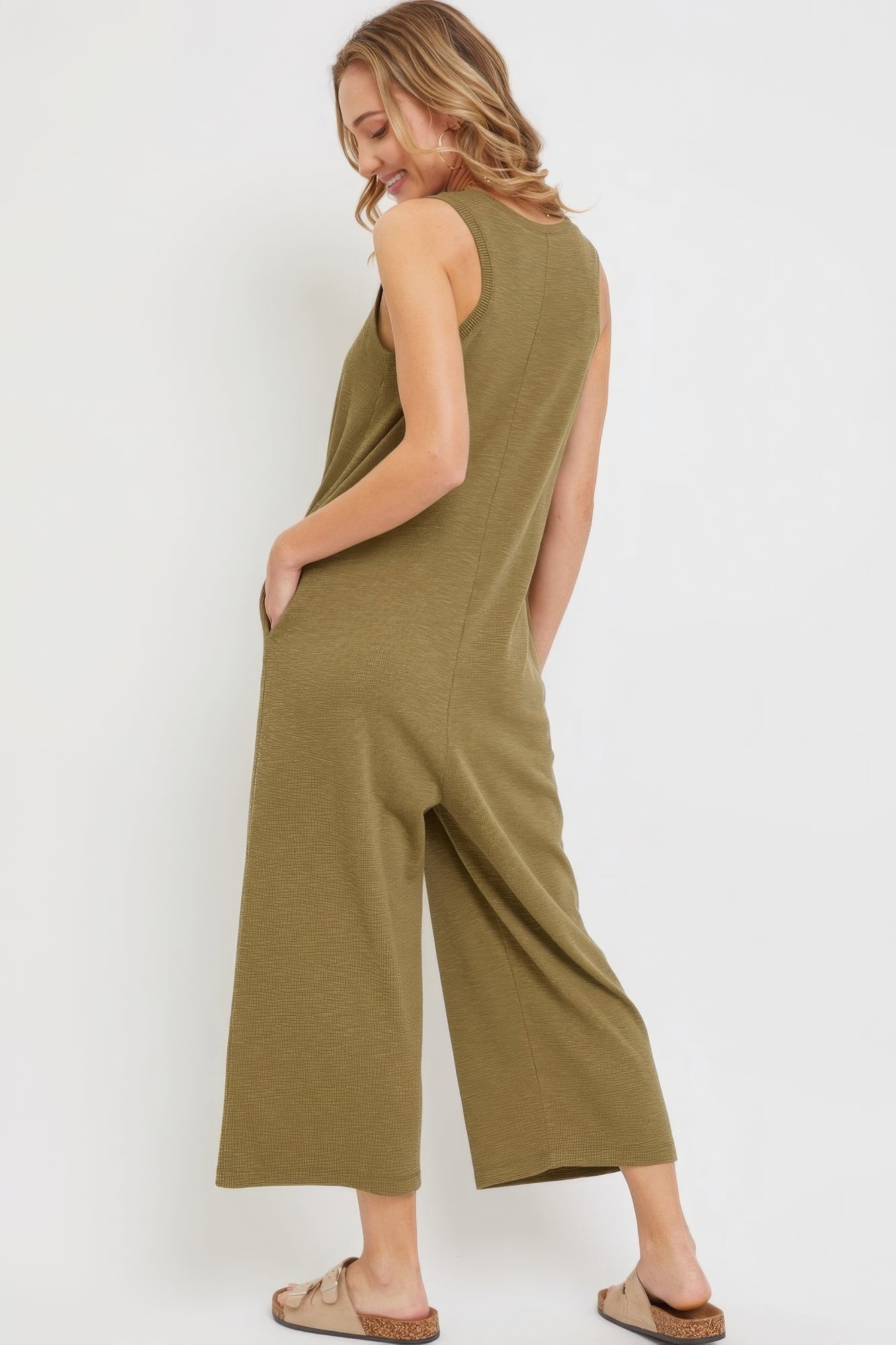 Woman wearing a sleeveless olive green casual buttondown jumpsuit with side pockets and relaxed fit.